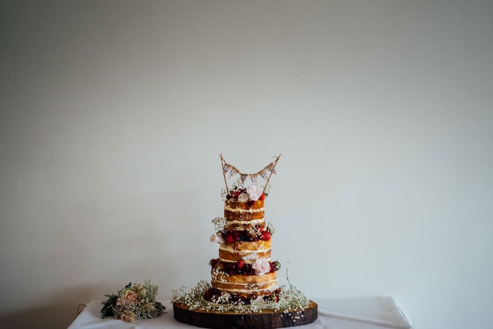 A shot of the naked sponge cake with 5 layers. The cake is filled with cream and berries and has a tiny string of bunting as a cake topper
