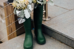A decor detail shot of some flowers poking  out of a green welly