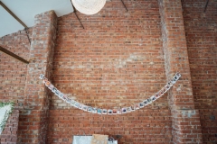 An image of the red brick wall on the inside of the red brick barn. There is a string of bunting on the wall. The bunting is made up of photos