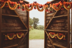 A shot through the door of the Really Rustic Barn showing part of the view beyond. Ther are orange floral garlands on the door.