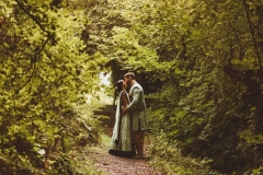 Couple in Indian wedding dress on the woodland walk. They are surrounded by green trees.