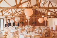 The Red Brick Barn all set up for a wedding reception with round tables and white linen. There is a larege white spherical abllonn in the centre of each table.