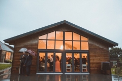 The Green Room Bar. The picture is taken from outside at dusk. The full length glass windows are lit up and you can see guests relaxing inside