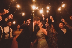 A sparkler exit. The couple kiss while holding up sparklers. They are surrounded by guests also with sparklers