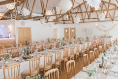 This is an image of the Red Brick Barn set up with long trestle tables. The centrepieces are pineapples on log slices. You can see the bar on the left hand side and the rustic beams in the ceiling.