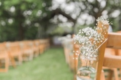 An image of the Oak Arbour set up for the ceremony. You can see the arbour and the 2 columns of rows of chairs.  In the foreground there is a jam jar strung with  twine  it is filled with gyp and is being used as a pew end.