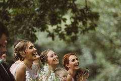 This is an image of 3 of the bridesmaids taken during the ceremony. They are shown from the shoulders up. They are surrounded by greenery. They are all smiling widely.