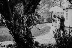 A black and white shot of a couple walking outside sheltering under an umbrella from the snow.