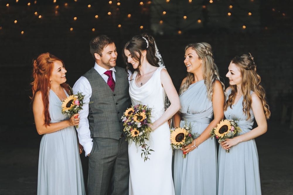 Amy and Kieran with their 3 bridemaids in pale blue dresses holding sunflower posies
