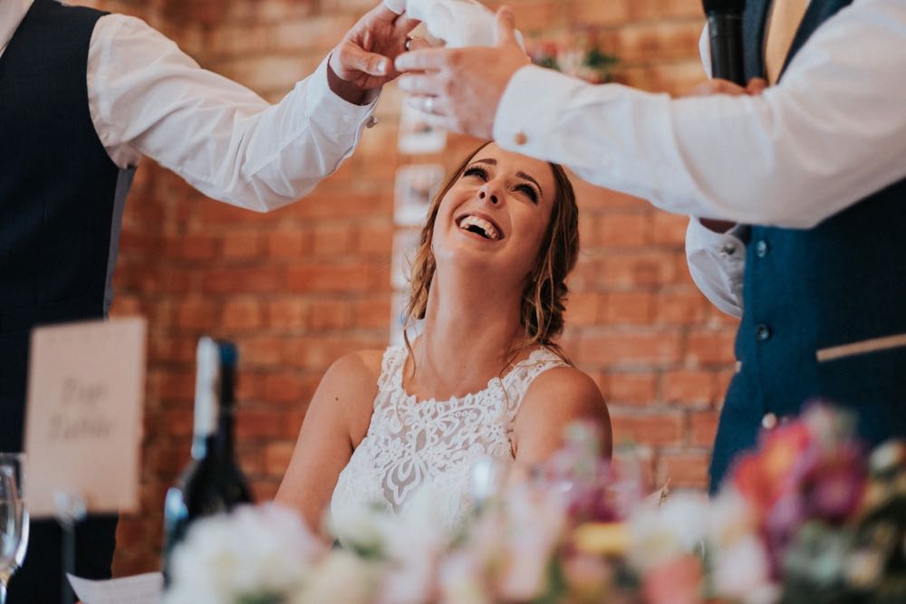 This is a close up of the bride smiling during the meal. You can see twi arms raised ina toast and she has her head thrown back and is laughing