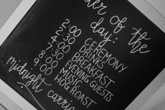 A cloe up picture of a blackboard sign with white writting with \"order of the day\". Ceremony, drinks, Breakfast, evening guests, music, hogroast