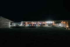 This is a night time shot of the Red Brick barn. It is dark outside and the barn is lit up. It is taken from quite a distance and the sky and foreground are dark but the light shines out of the windows