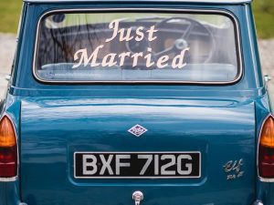 This image shows the rear of a Riley Elf car. It is a close-up shot of the back of the car and there is a saying in white writing on the rear window saying just married. Riley elf is blue in colour and the registration number is VXF712G.