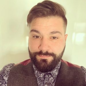 A head an shoulders shot of David our events manager. David is wearing floral shirt and waistcoat. He has brown hair swept over in a side parting and a beard.