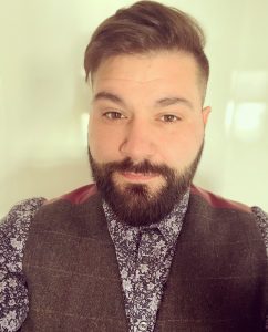 A head an shoulders shot of David our events manager. David is wearing floral shirt and waistcoat. He has brown hair swept over in a side parting and a beard.