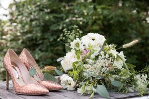 Pair of pink stiletto wedding shoes with white and pink bouquet sitting on a wooden table